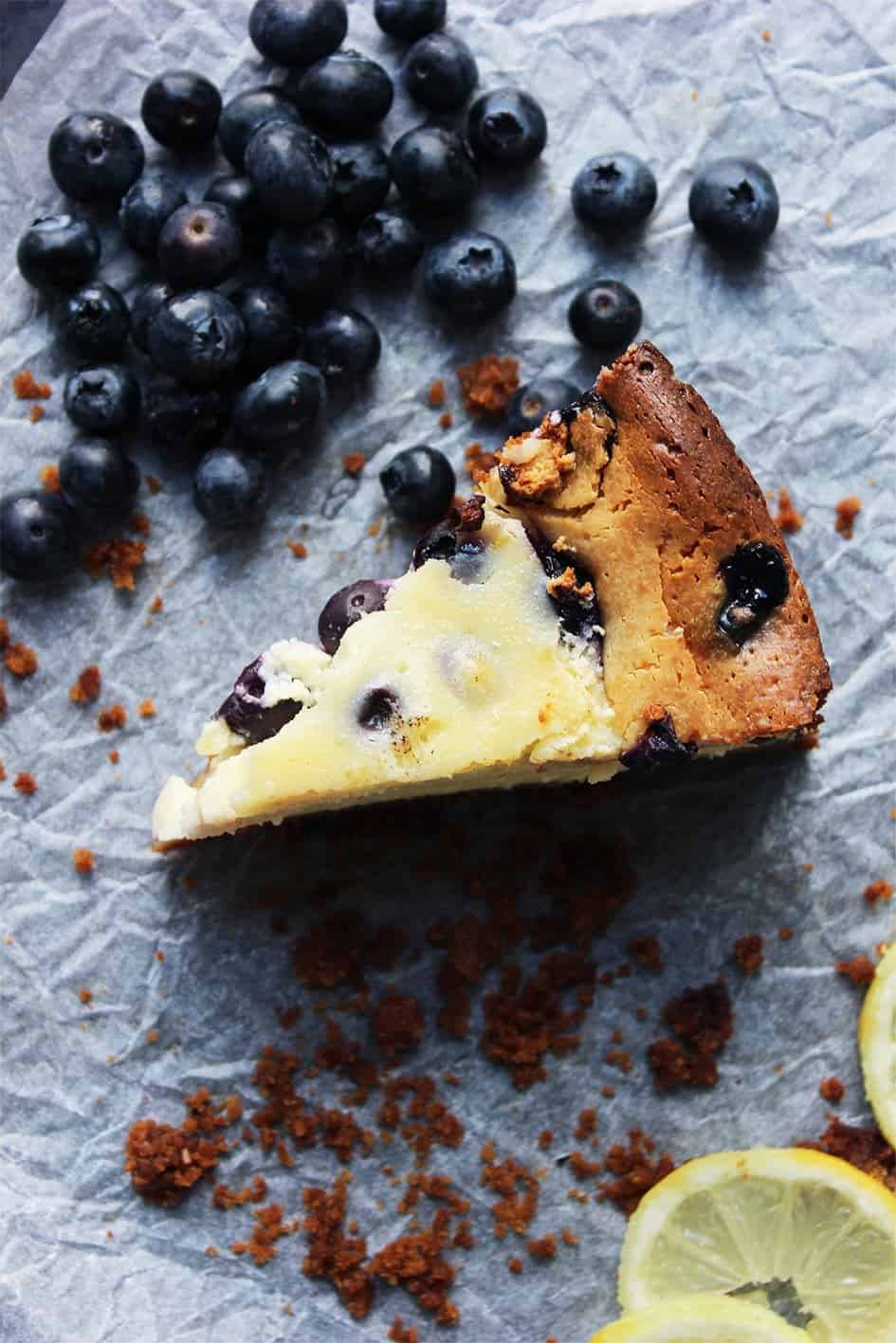 A slice of Baked Lemon & Blueberry Cheesecake on a piece of parchment