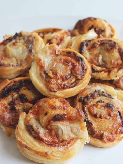 Bacon and cheese puff pastry pinwheels stacked on a white plate