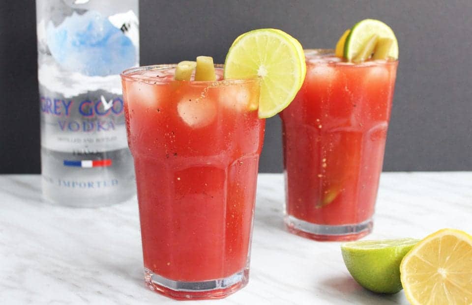 Two caesar drinks with lemon and lime garnish.