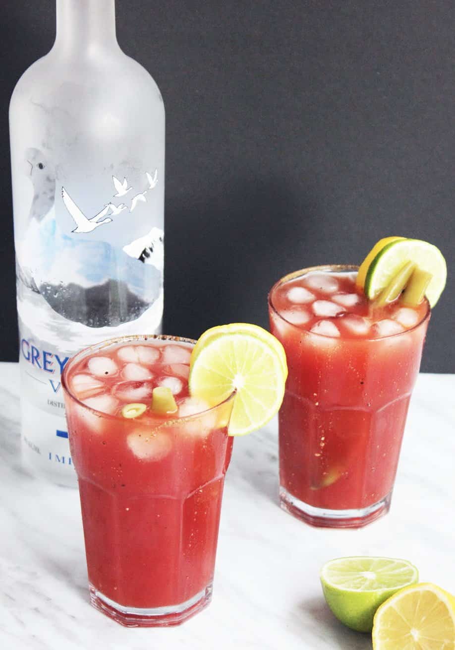Two caesar drinks with lemon and lime garnish.