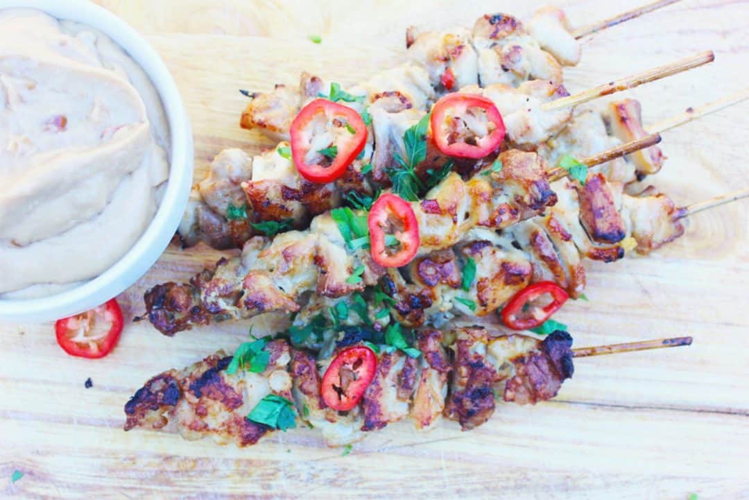 skewers of crispy chicken satay with peanut dipping sauce on a wooden serving board