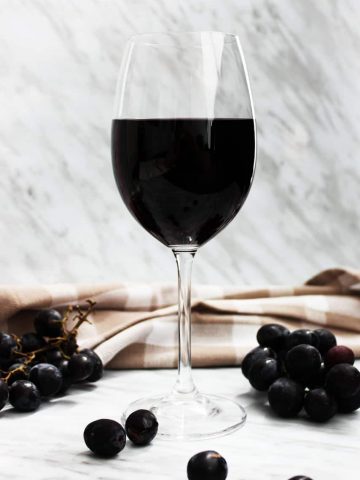 A glass of red wine on a marble backdrop with bunches of grapes
