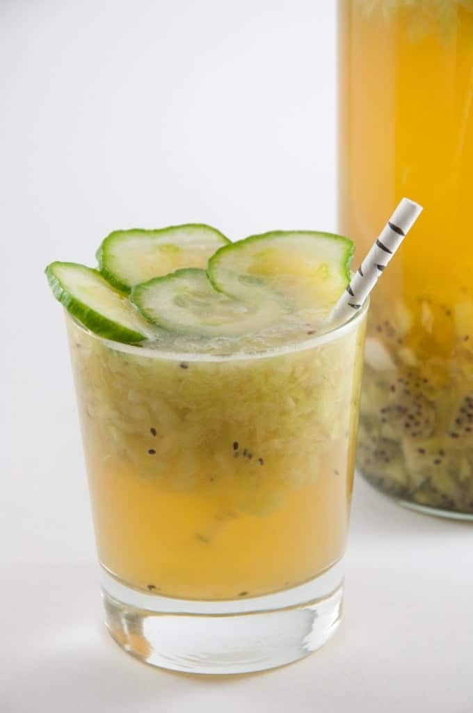 A green destiny cocktail in a tumbler garnished with cucumbers