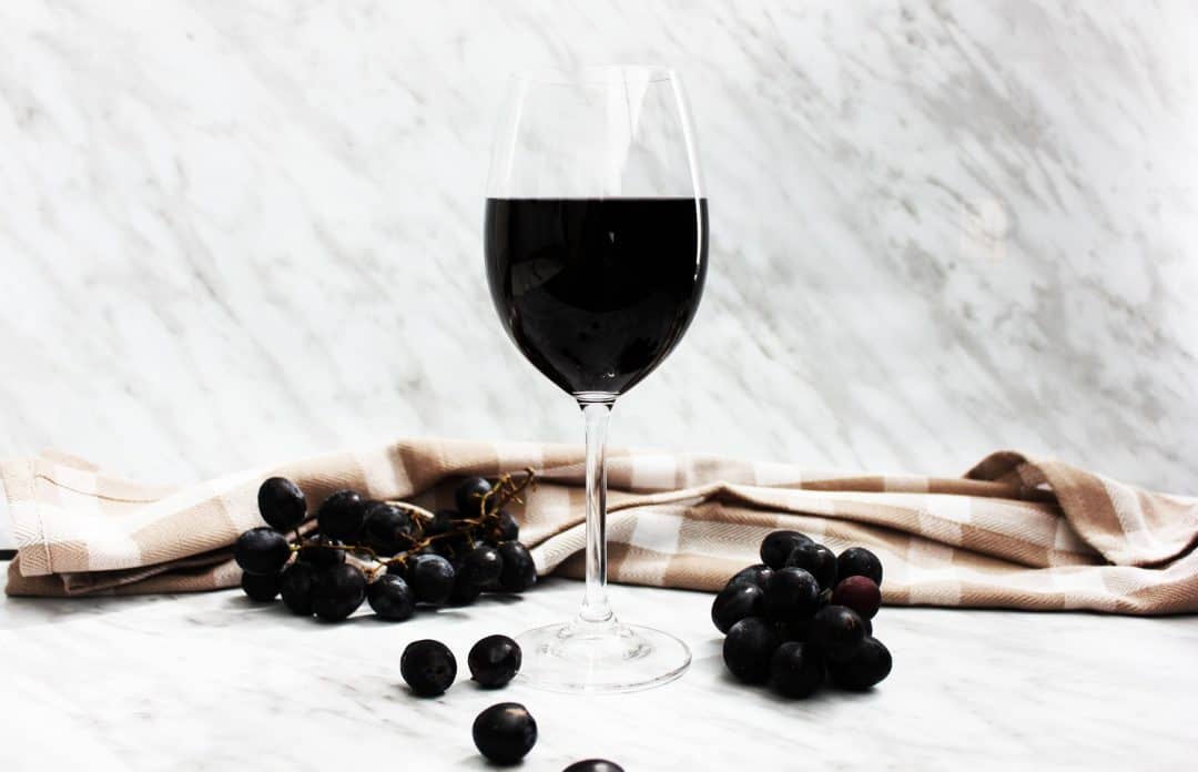 A glass of red wine on a marble backdrop with bunches of grapes