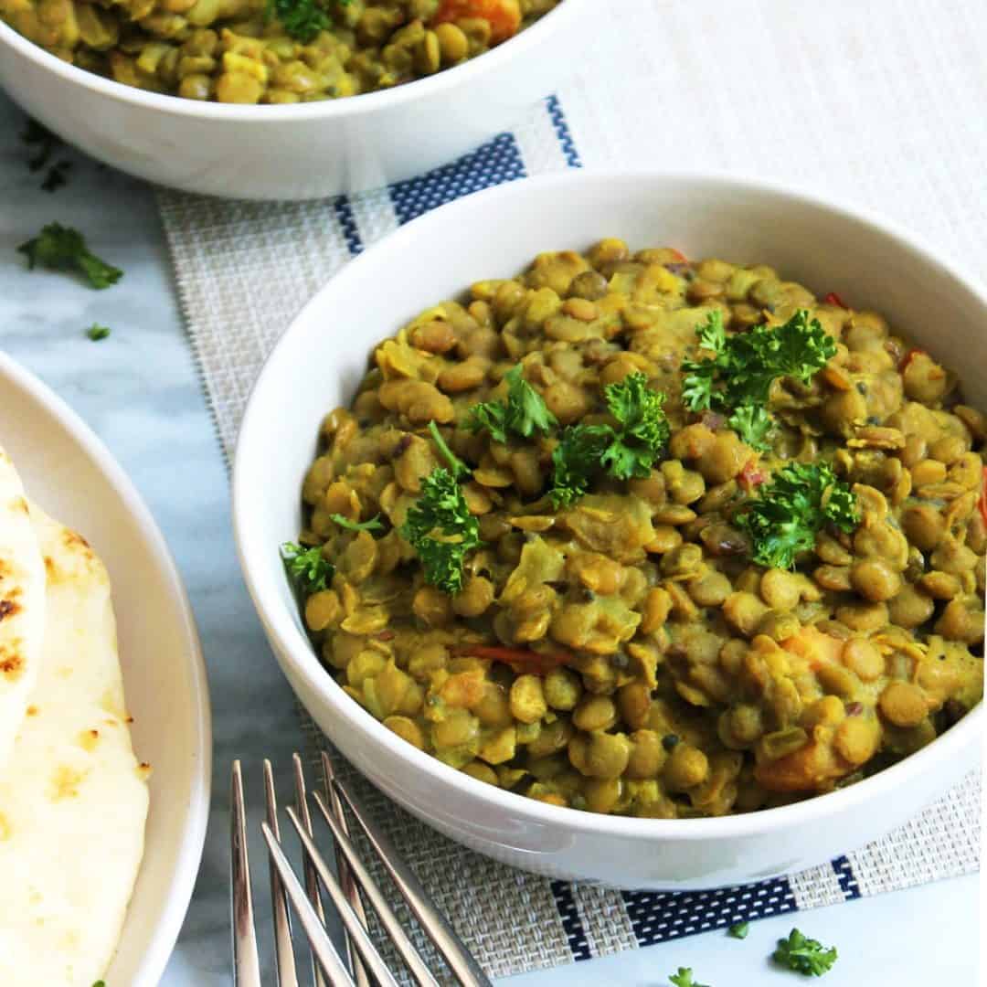 A bowl of green lentil daal with two forks on a white and blue mat