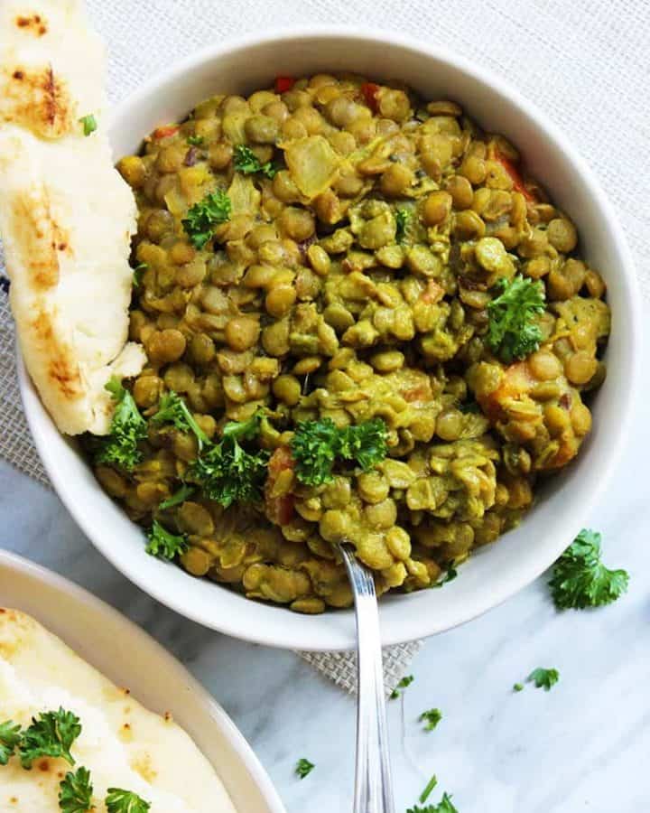 Overhead shot of green lentil daal in a bowl with a piece of ripped naan bread in the bowl