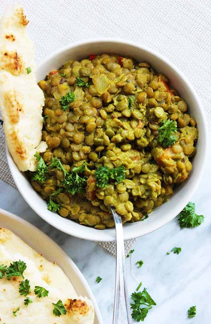 Overhead shot of green lentil daal in a bowl with a piece of ripped naan bread in the bowl