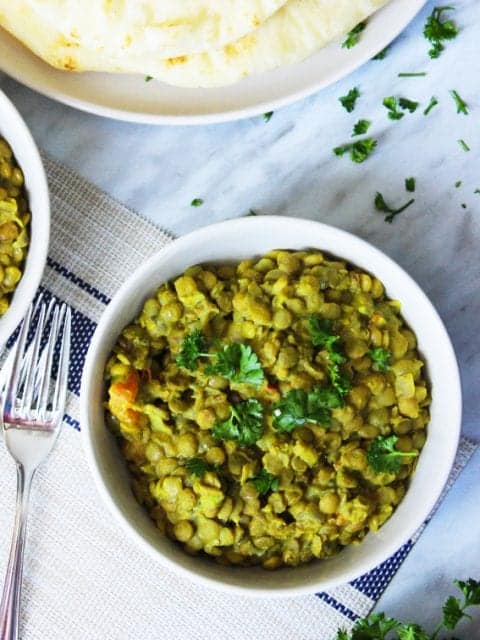 overhead shot of a bowl of green lentil daal, next to naan bread with a fork on the table