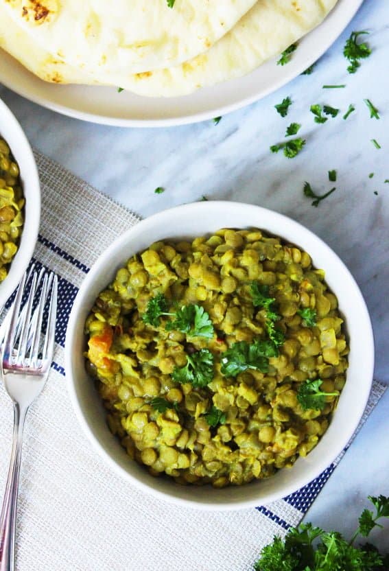 overhead shot of a bowl of green lentil daal, next to naan bread with a fork on the table