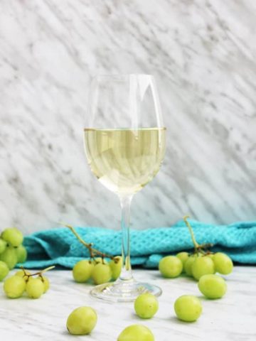 A glass of white wine with white grapes scattered around