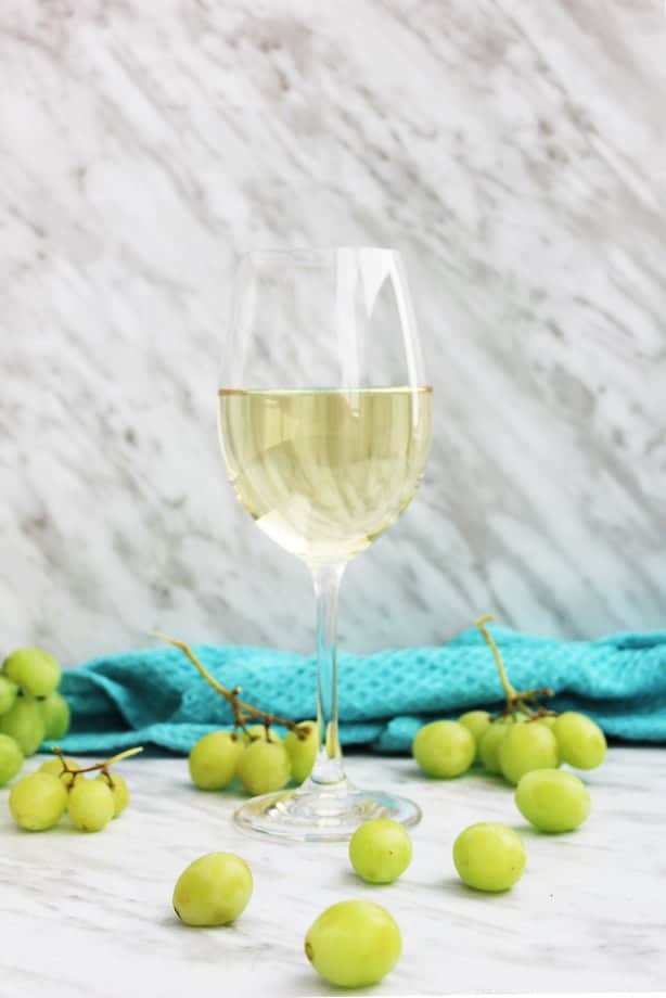 A glass of white wine with white grapes scattered around
