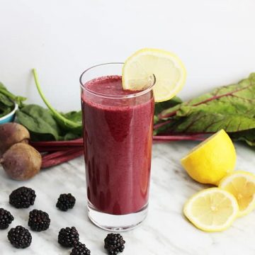 A beet smoothie in a tall glass on a white work surface