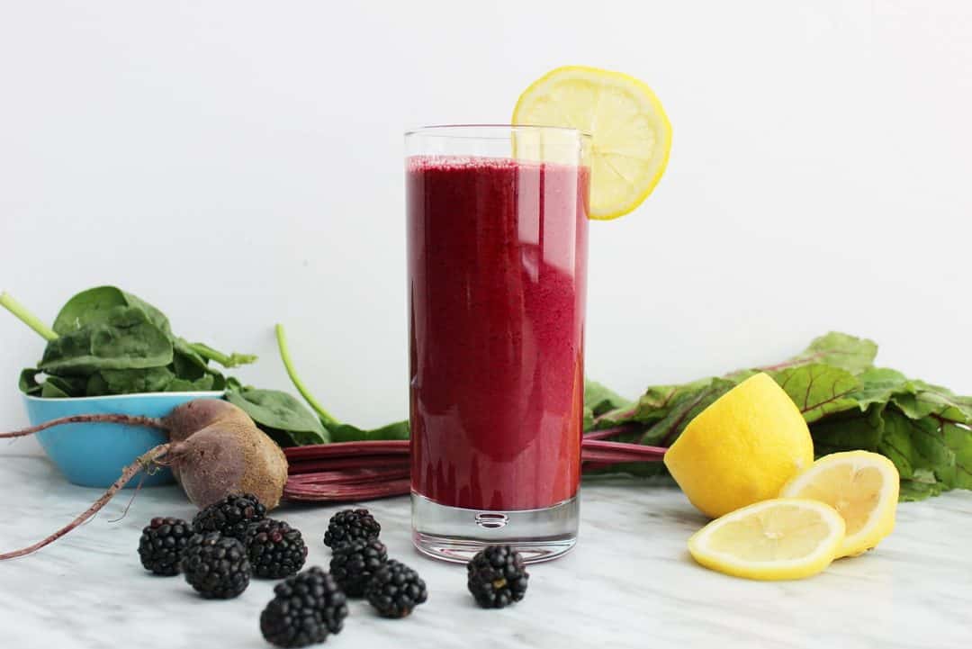 A side shot of a beet smoothie surrounded by the raw ingredients