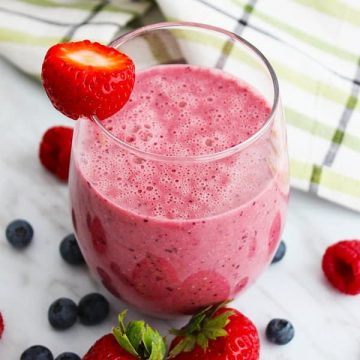 A Berry oat smoothie on a marble work surface, with fresh fruit around it
