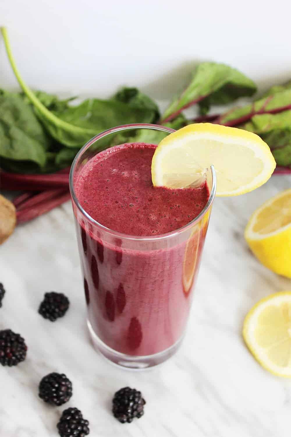 A tall glass of beet smoothie, garnished with a lemon slice