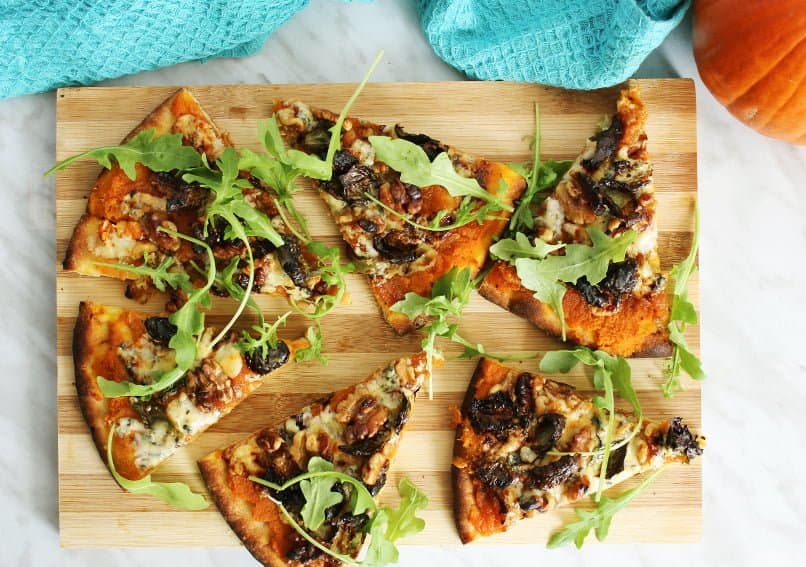 Top down shot of blue cheese pizza with pumpkin on a wooden chopping board
