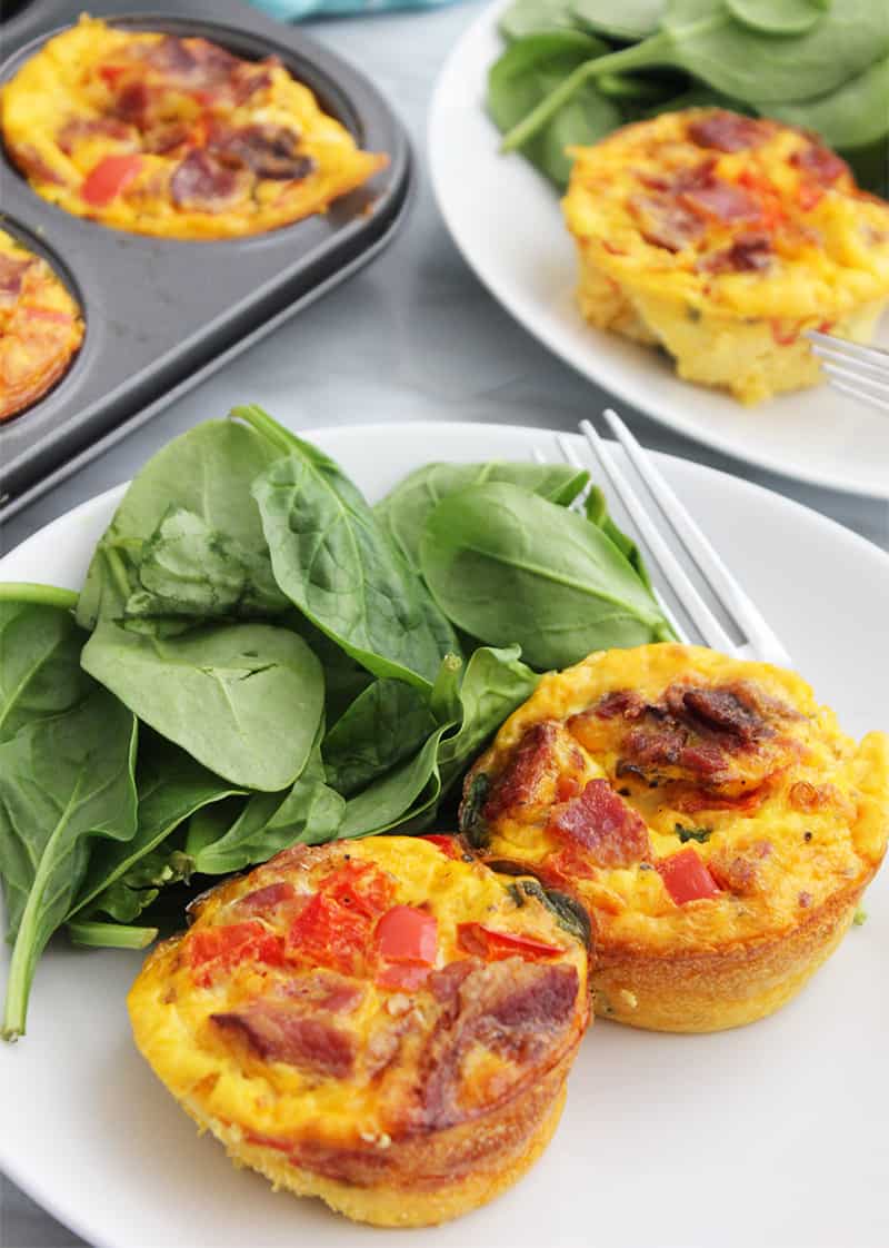 Two egg muffins on a white plate with fresh spinach