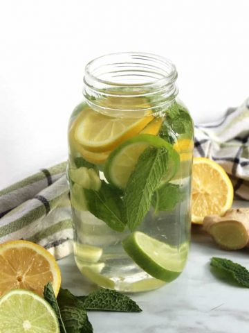 A mason jar of infused water with fresh lemon, lime and mint inside it
