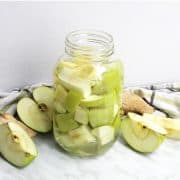 Green Apple Vodka in a jar next to sliced apples
