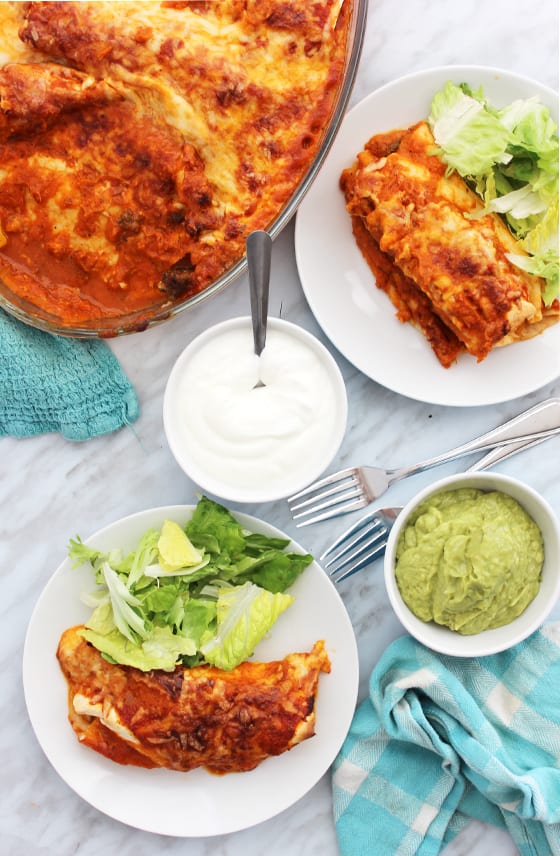 Top down shot of enchiladas served with sour cream and guacamole