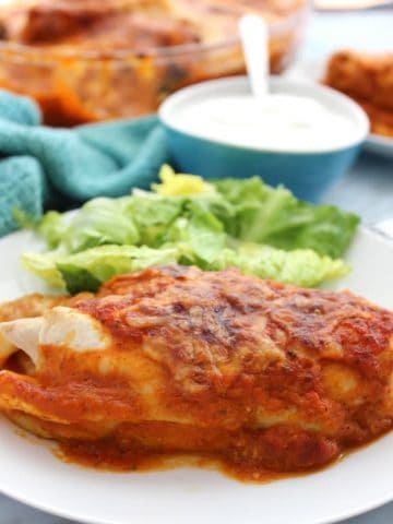 An enchilada on a white plate with sour cream
