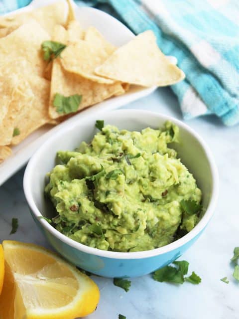 A bowl of guacamole next to a plate of tortilla chips