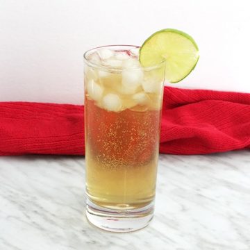 A spiced rum cocktail, garnished with lime, on a marble work top.
