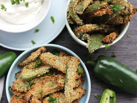 Top shot of two bowls of crispy jalapeno fries with sour cream dip and fresh herbs