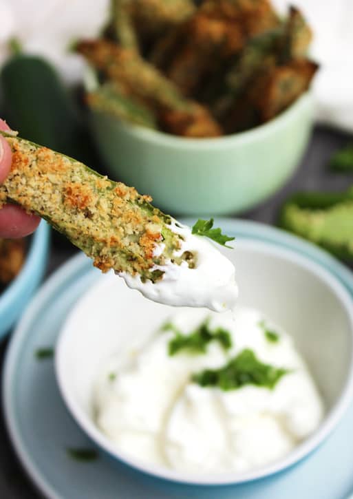 A crispy jalapeno fry dipped in sour cream and held towards camera