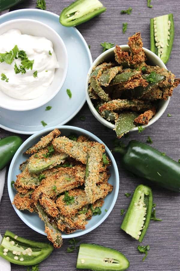 Top shot of two bowls of crispy jalapeno fries with sour cream dip and fresh herbs