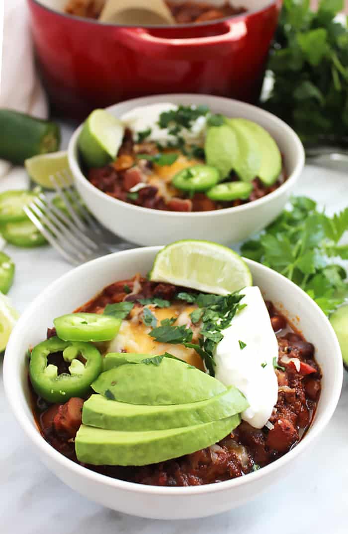 Two bowls of roasted ground beef chili with avocado, jalapenos and sour cream