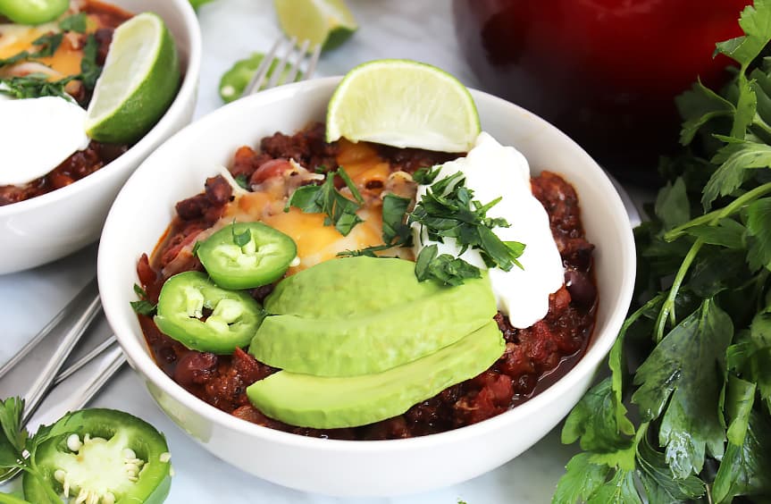 Close up of roasted ground beef chil in a white bowl with toppings