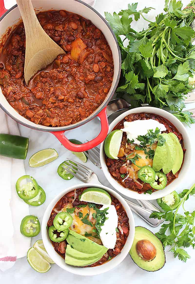 Two bowls of roasted ground beef chili and chili in a red pot