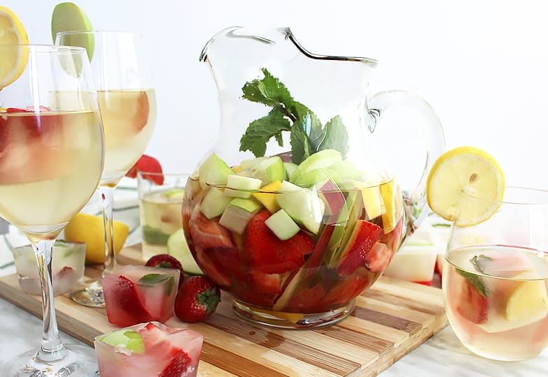 A jug of white wine sangria on a board with wine glasses