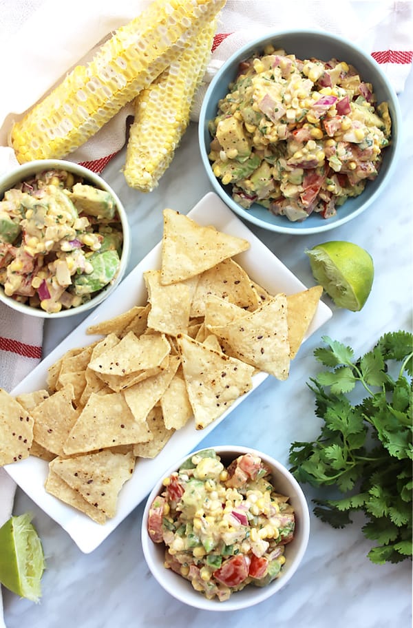 Three bowls of corn salsa with avocado served with tortilla chips