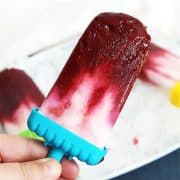 A cherry and yogurt popsicle being held towards camera