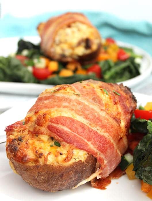 A baked potato filled and wrapped in bacon, served on a white plate