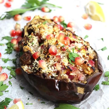A stuffed eggplant topped with pomegranate seeds and fresh herbs