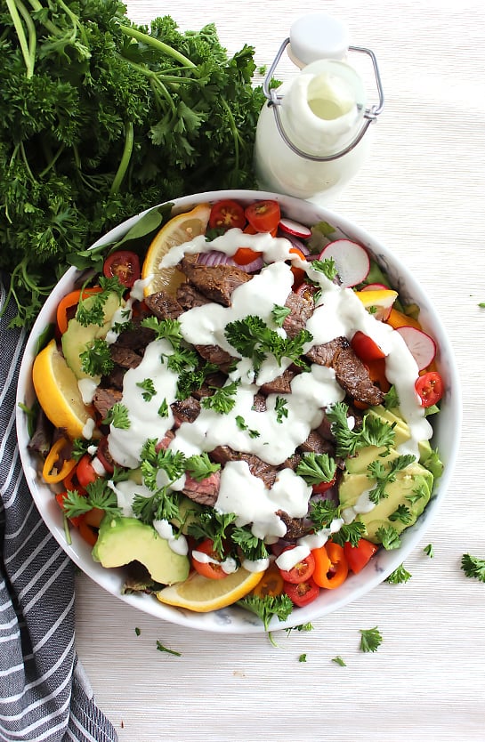 A bowl of steak salad on a white surface