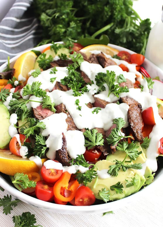 Steak salad in a large white bowl with fresh herb garnish