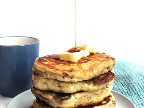 A stack of savory pancakes on a plate with maple syrup being drizzled on top