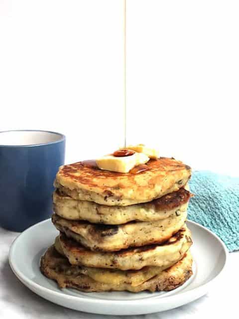 A stack of savory pancakes on a plate with maple syrup being drizzled on top