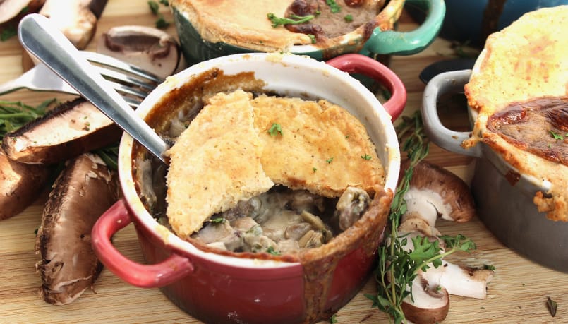 Close up of a vegetarian mushroom pot pie in a small red casserole with the crust broken