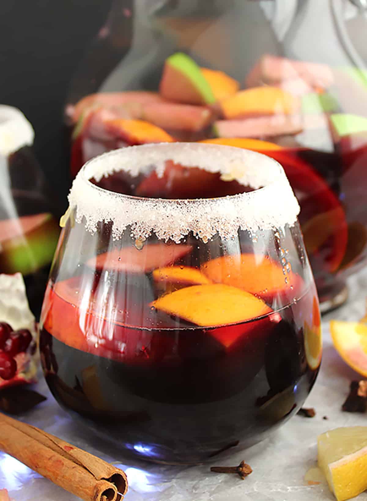 A glass of red wine sangria in front of a jug