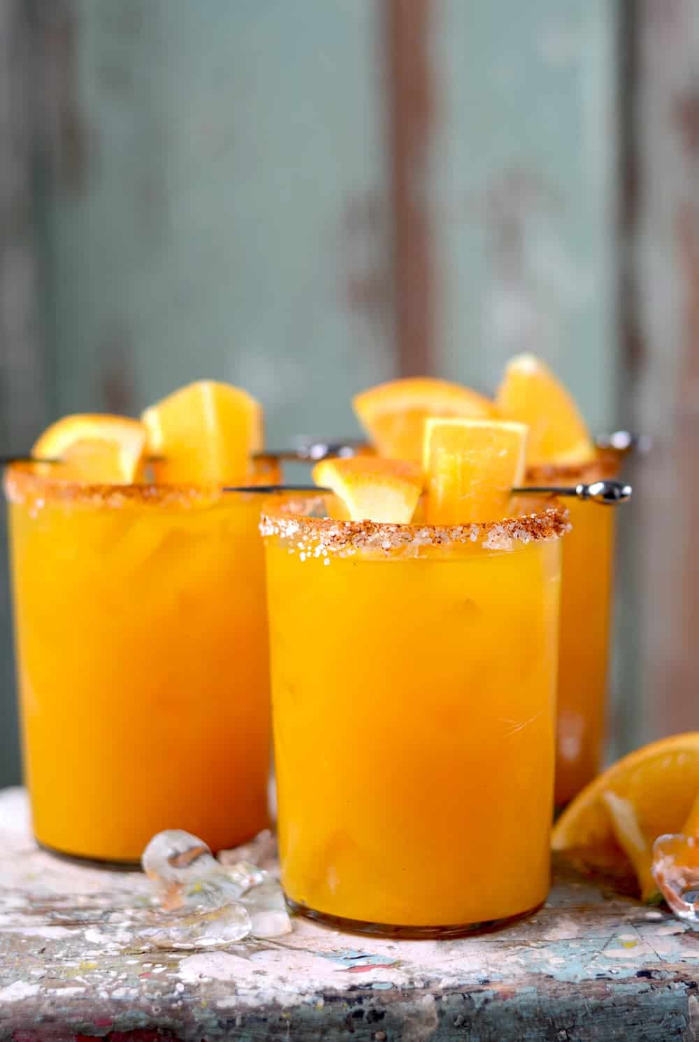 Three orange turmeric margaritas in tall glasses