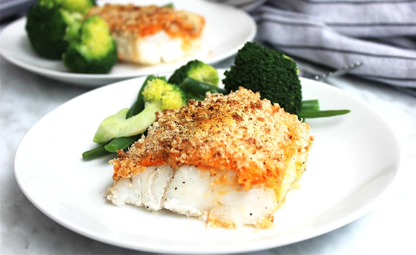 Crispy baked cod served on a white plate with green veggies