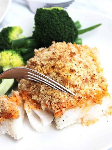A piece of crispy baked cod being cut into with a fork