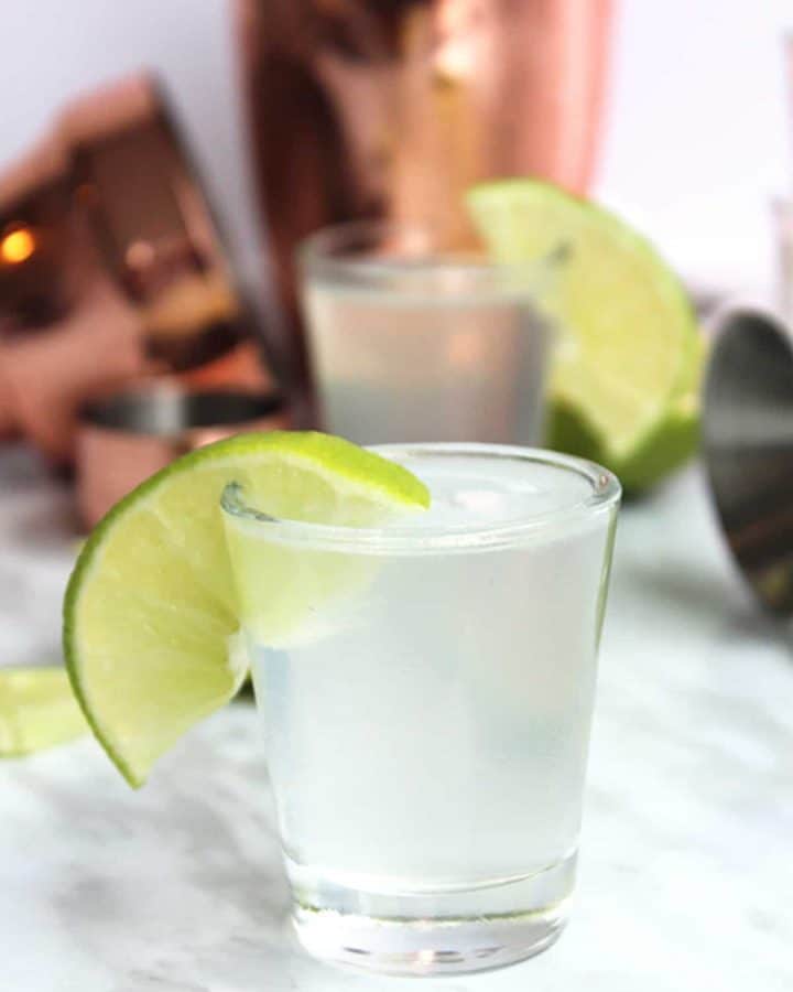 A gin shot in front of a gold cocktail shaker