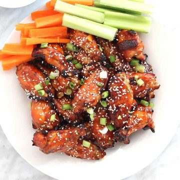 Wings topped with sesame seeds and green onions on a white plate