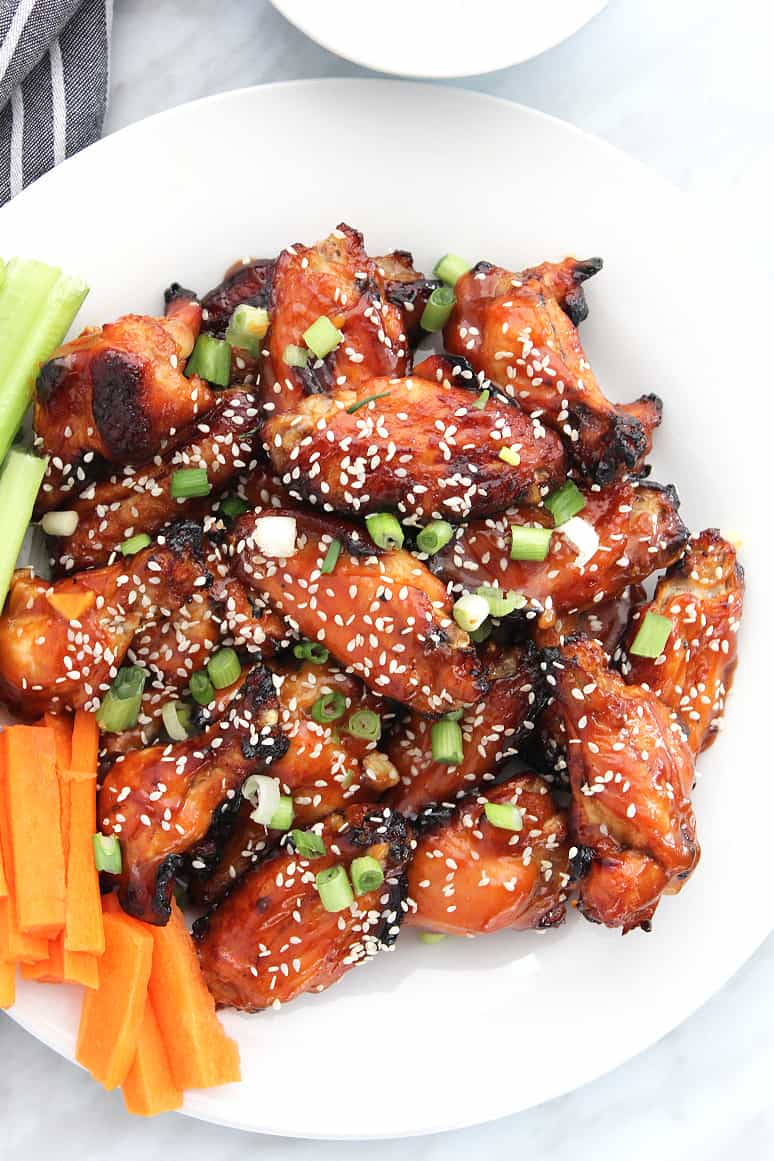 Sticky chicken wings served on a white plate with carrot and celery sticks
